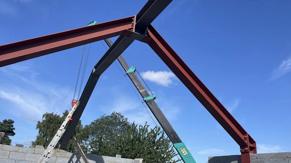 Structural steel roof frame lifted into place against a blue sky